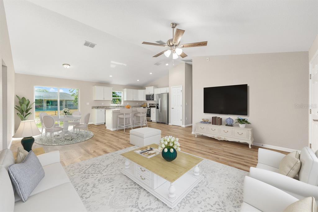 A bright, open-concept living room and kitchen featuring light wood floors and white cabinetry — 14362 SW 30TH PLACE, OCALA, FL
