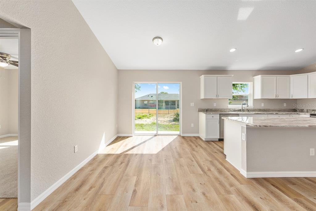 A kitchen and dining area with light wood-look flooring, white cabinets, and sliding glass doors — 14362 SW 30TH PLACE, OCALA, FL