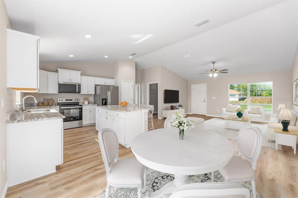 An open-concept kitchen, dining area, and living room featuring white cabinetry, an island, and wood-look flooring — 14362 SW 30TH PLACE, OCALA, FL