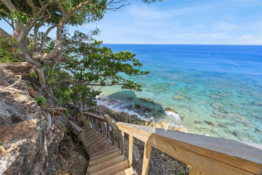 A wooden staircase with a railing leads down a rocky cliff toward the turquoise ocean — Lot 4 IBIZA ST, RD 107 KM 2.7, AGUADILLA, PR