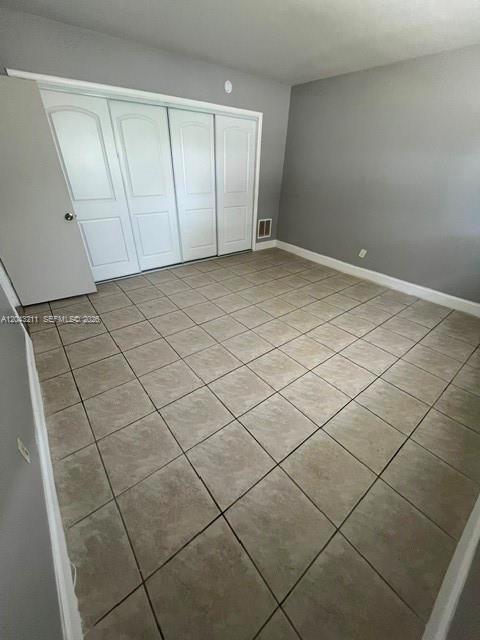 An empty bedroom features gray walls, a tiled floor, and a four-panel white closet door — FORT LAUDERDALE, FL
