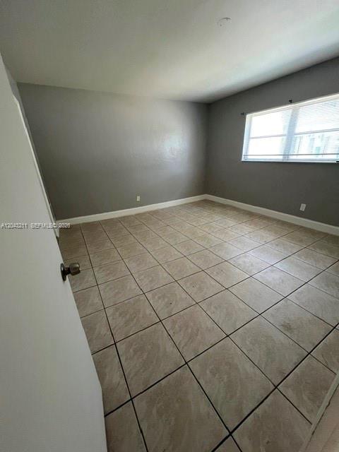 An empty room with gray walls, tiled flooring, and a window with white blinds — FORT LAUDERDALE, FL