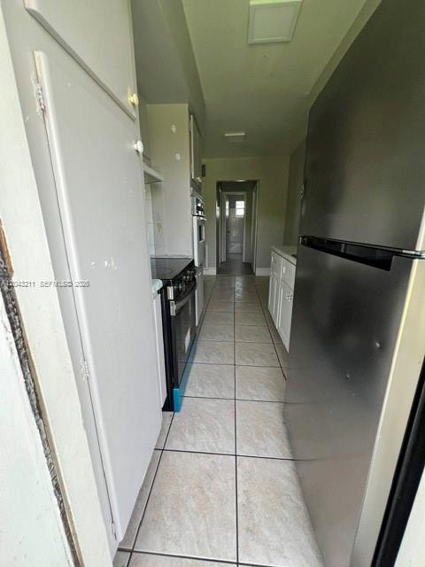 A narrow galley kitchen features light-colored tile flooring, white cabinetry, and stainless steel appliances — FORT LAUDERDALE, FL