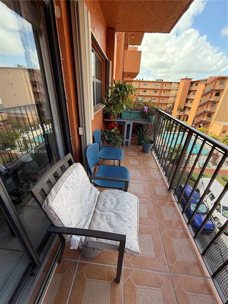 A balcony with tiled flooring features outdoor seating, potted plants, and a view of buildings — 1800 W 54th St # 309, Hialeah FL 33012, HIALEAH, FL