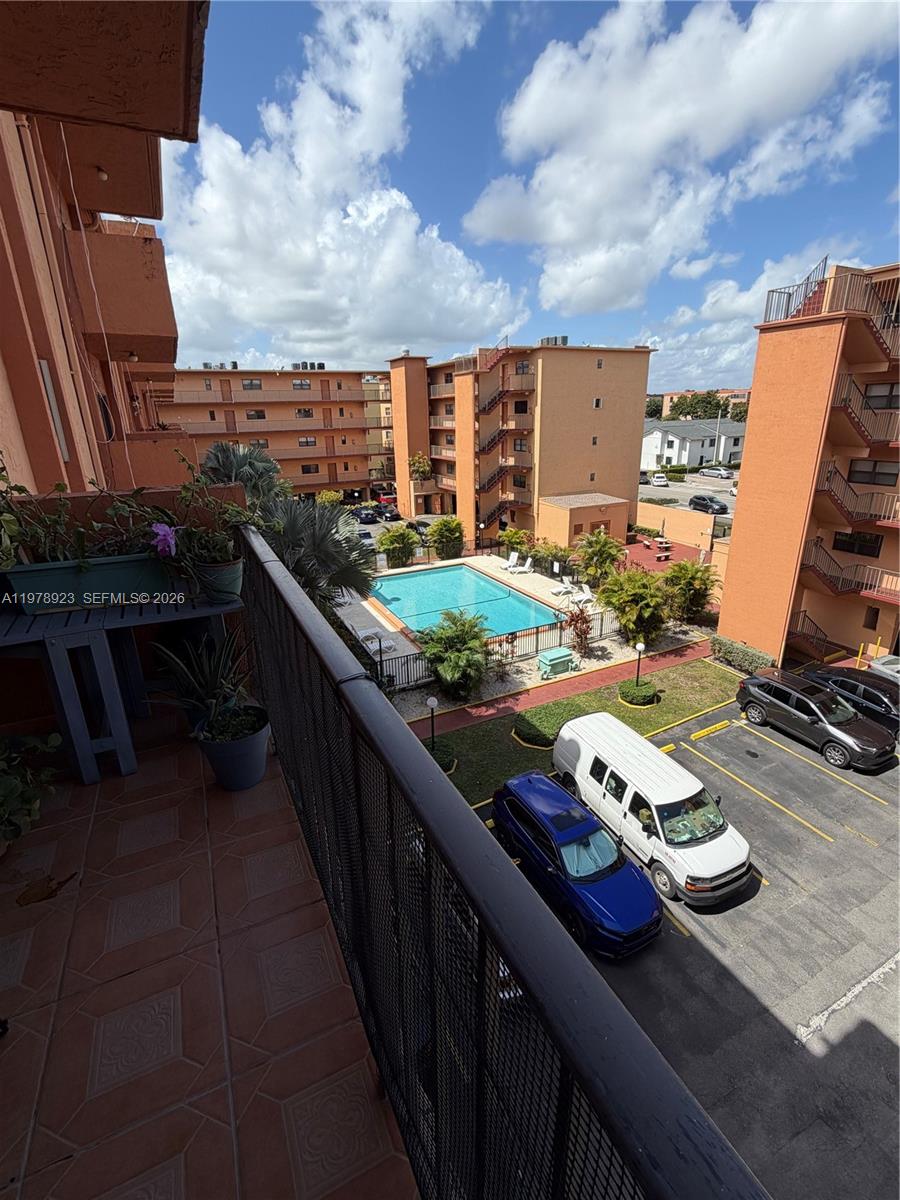 A balcony overlooks a swimming pool, parking lot, and apartment buildings under a blue sky — 1800 W 54th St # 309, Hialeah FL 33012, HIALEAH, FL