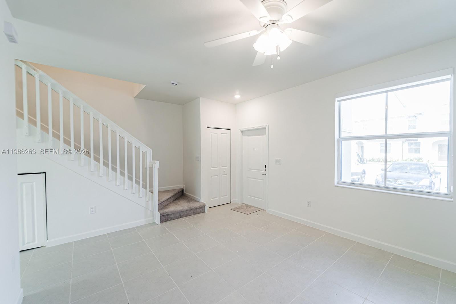 A bright room features white walls, tile flooring, a staircase, and a ceiling fan — 2620 SE 28th Dr, Homestead FL 33035, HOMESTEAD, FL