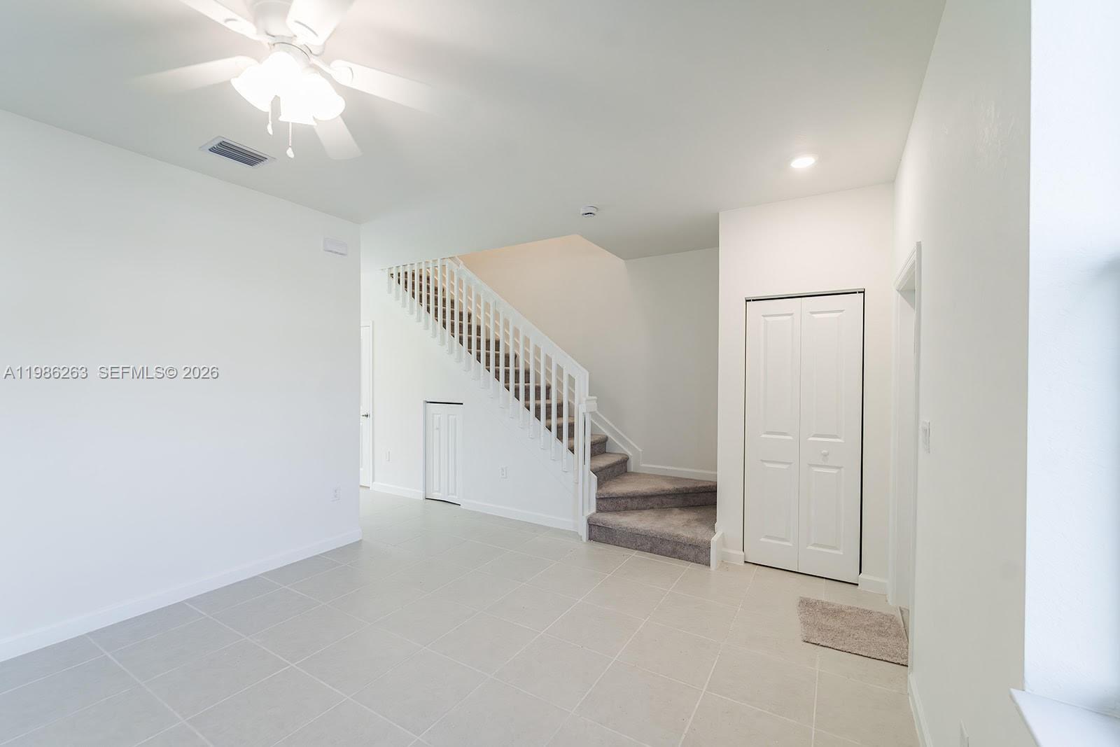 A room with light tile flooring, a carpeted staircase, and white walls — 2620 SE 28th Dr, Homestead FL 33035, HOMESTEAD, FL