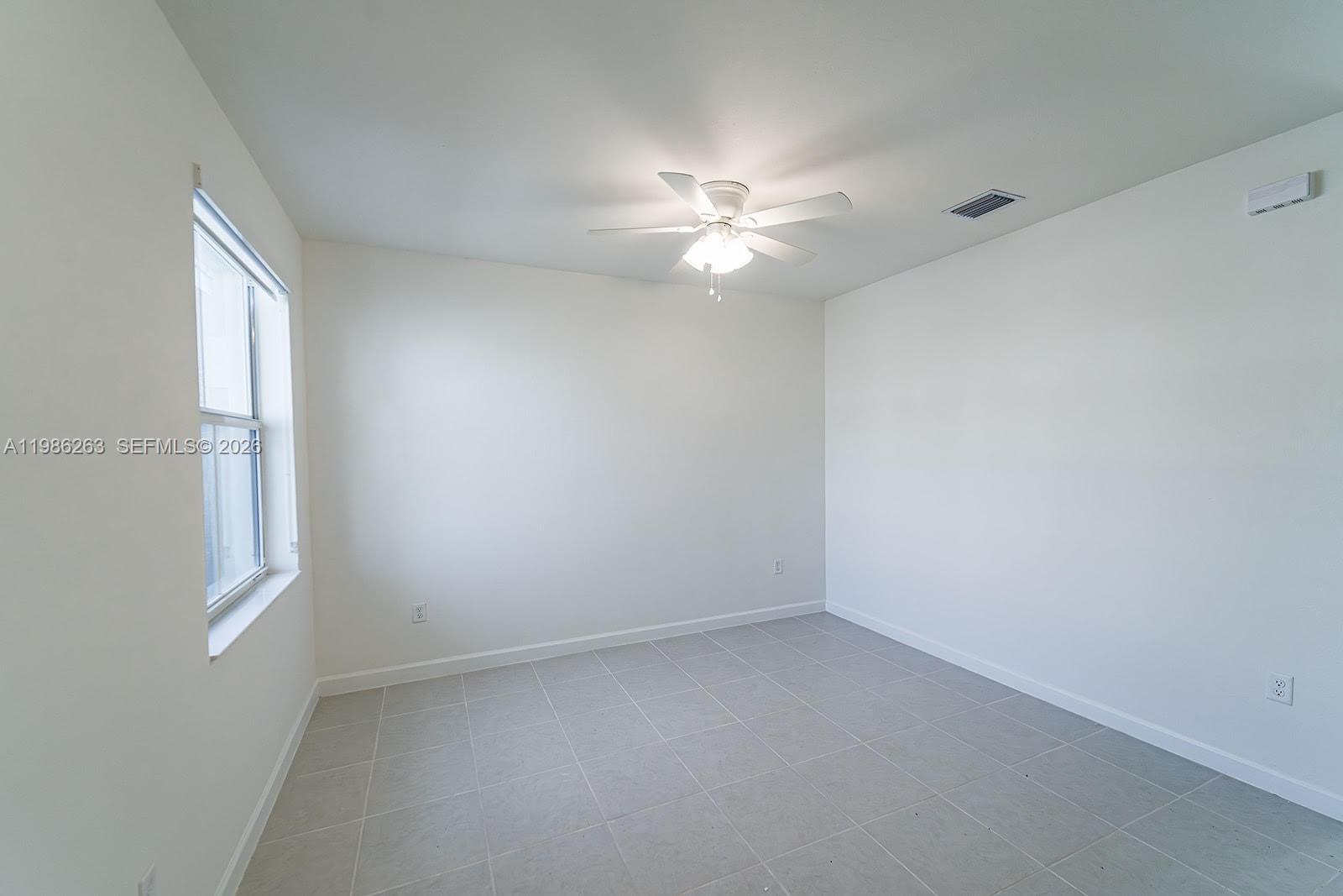 An empty bedroom features white walls, gray tile flooring, and a ceiling fan — 2620 SE 28th Dr, Homestead FL 33035, HOMESTEAD, FL