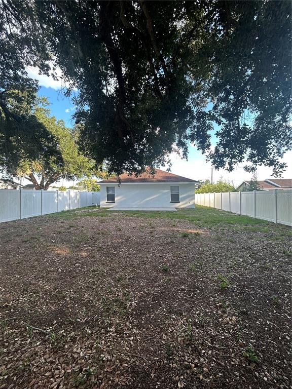 The backyard of a house features a white fence, a concrete patio, and large trees — 702 LEMON AVE, DUNDEE, FL