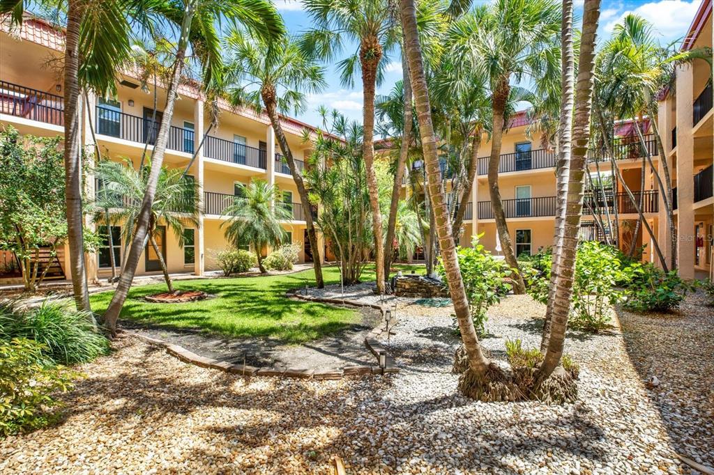 A courtyard with palm trees, a grassy lawn, and gravel landscaping between apartment building wings — 8911 BLIND PASS ROAD UNIT 120, ST PETE BEACH, FL