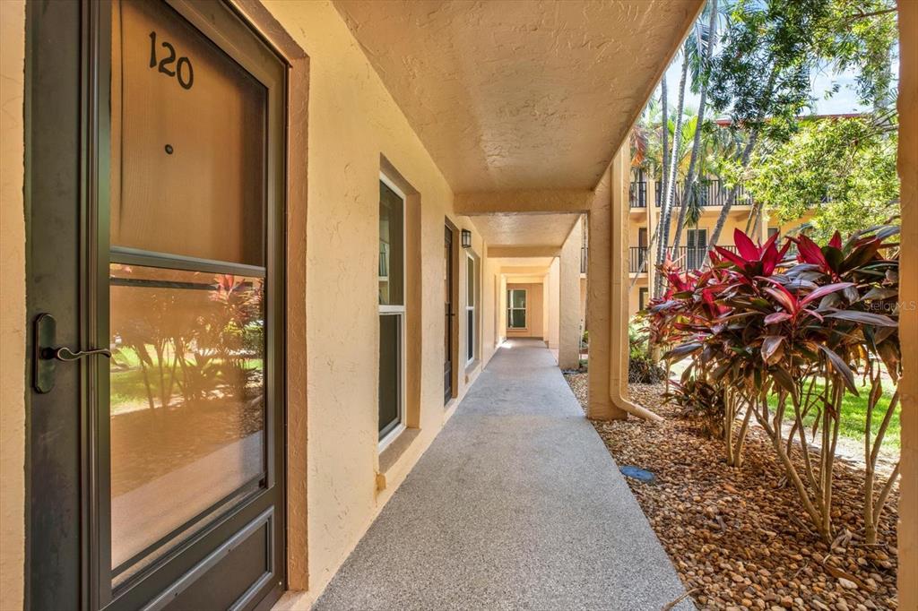 An outdoor covered walkway leads past apartment unit 120 with a screen door — 8911 BLIND PASS ROAD UNIT 120, ST PETE BEACH, FL