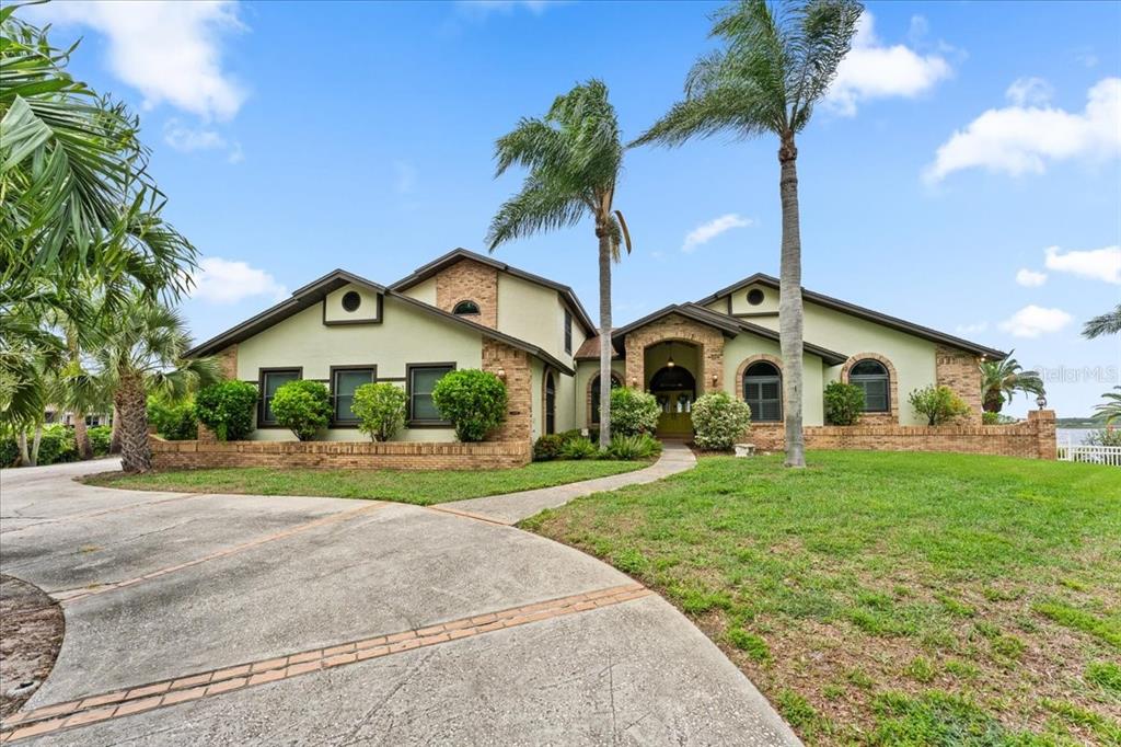 A two-story house with a brick and light green exterior features a curved concrete driveway — 1589 MARY LANE, TARPON SPRINGS, FL