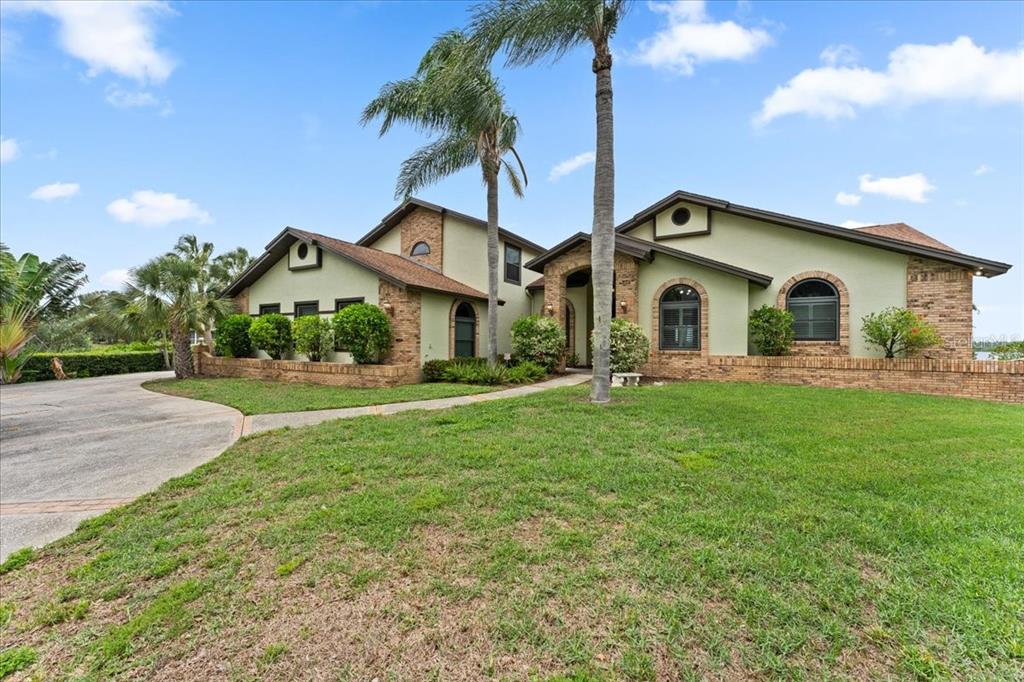 A two-story house with light green stucco, brick accents, and palm trees in the front yard — 1589 MARY LANE, TARPON SPRINGS, FL