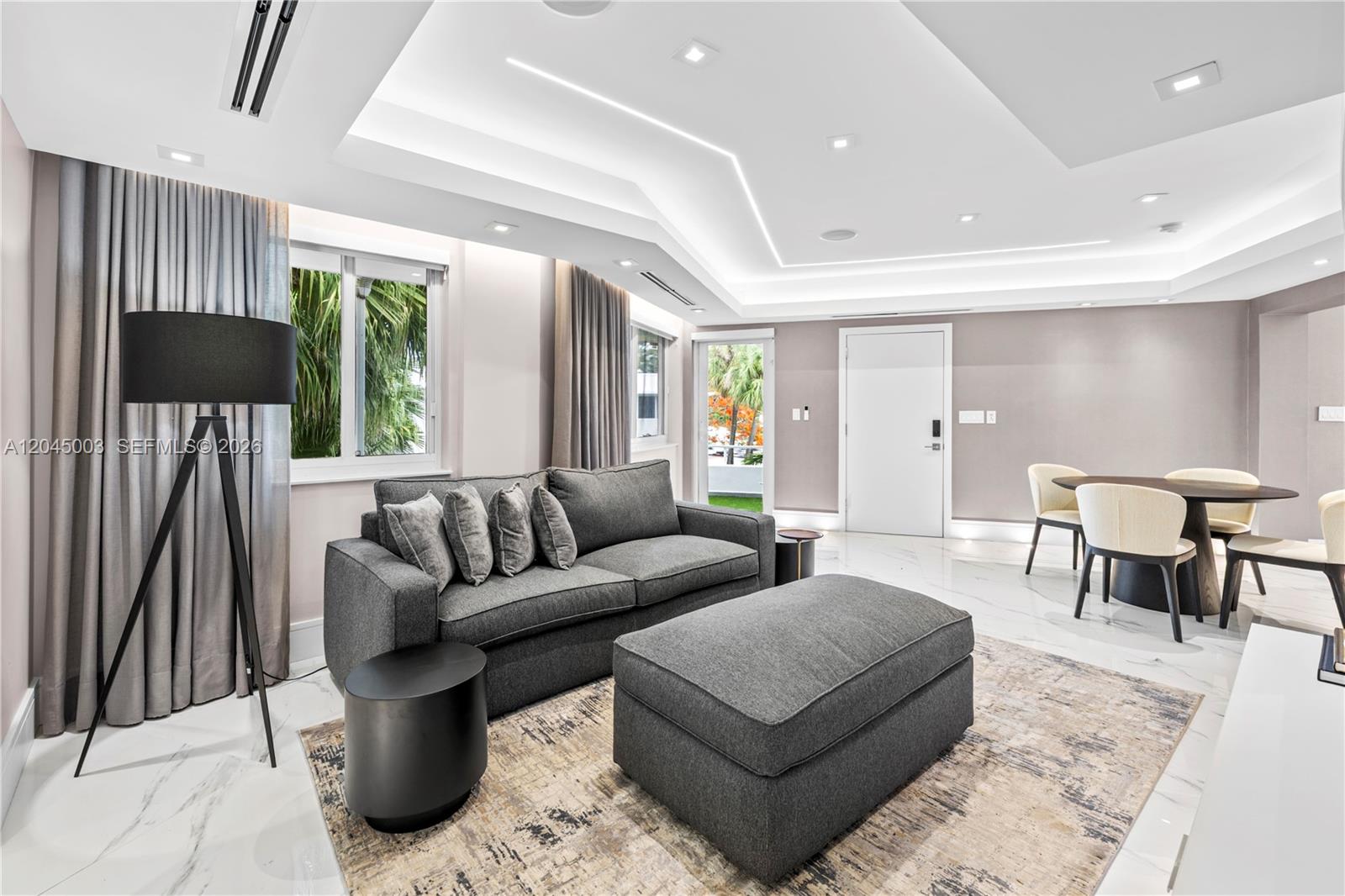 A modern living room features a gray sofa, matching ottoman, and a dining area — 10190 Collins Ave # 203, Bal Harbour FL 33154, BAL HARBOUR, FL