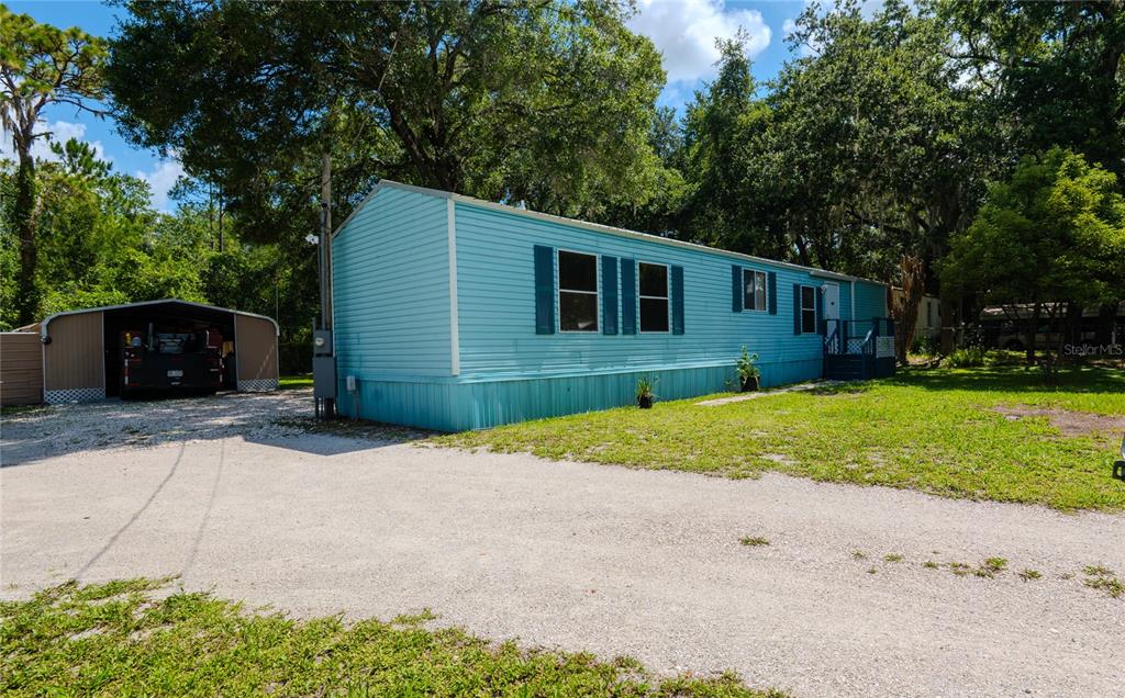 A light blue mobile home sits on a gravel lot with a detached metal carport — 312 DONALD LANE, WINTER HAVEN, FL