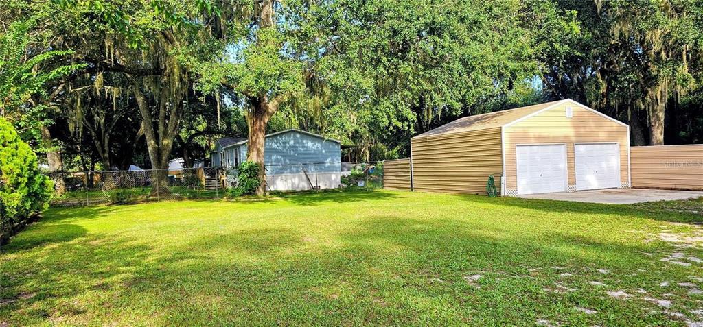 A grassy yard features a detached two-car garage and a mobile home under large trees — 312 DONALD LANE, WINTER HAVEN, FL