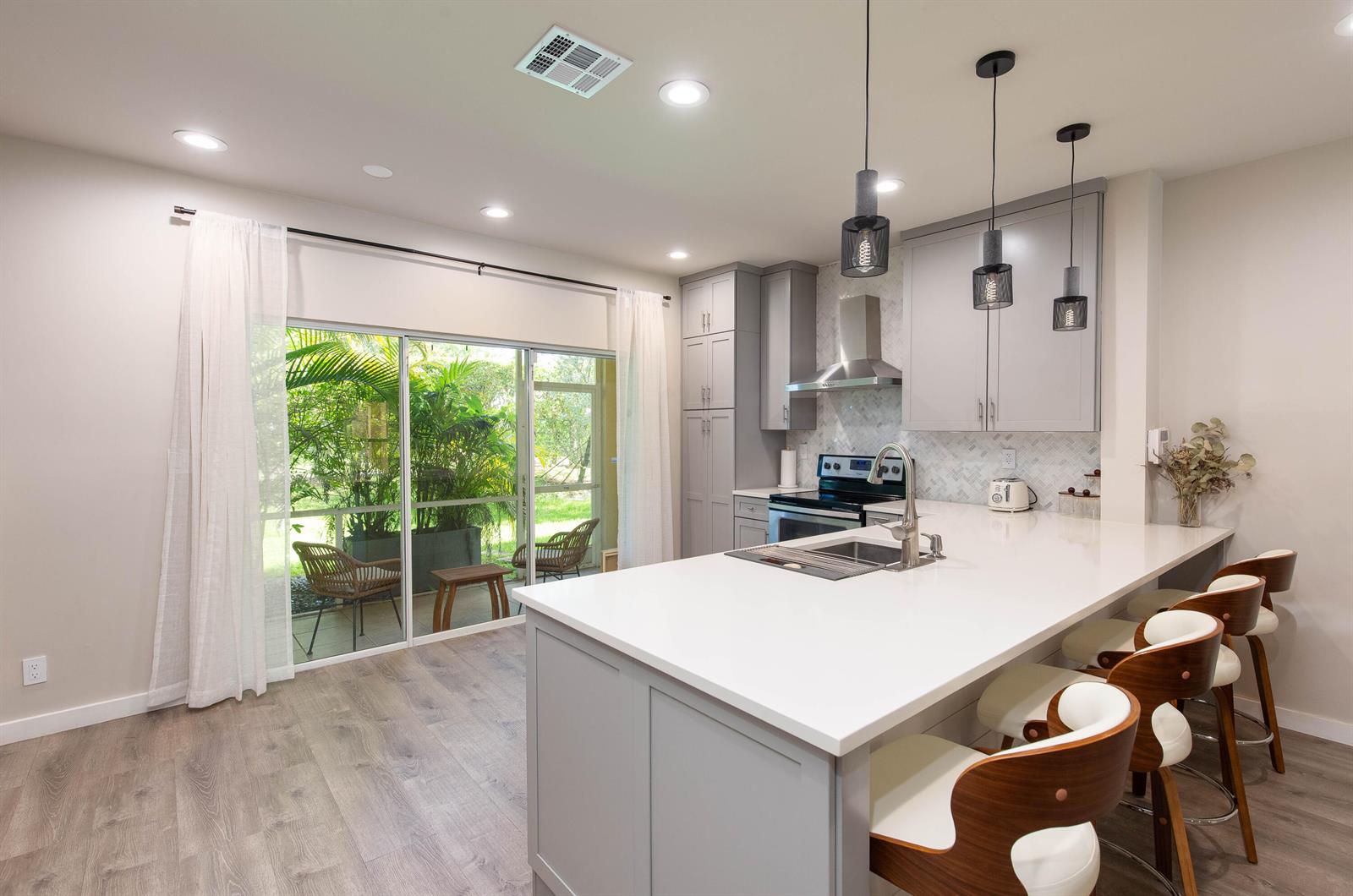 A modern kitchen features gray cabinets, a white quartz island, and a sliding glass door — 13792 Creston Place, Wellington FL 33414, WELLINGTON, FL