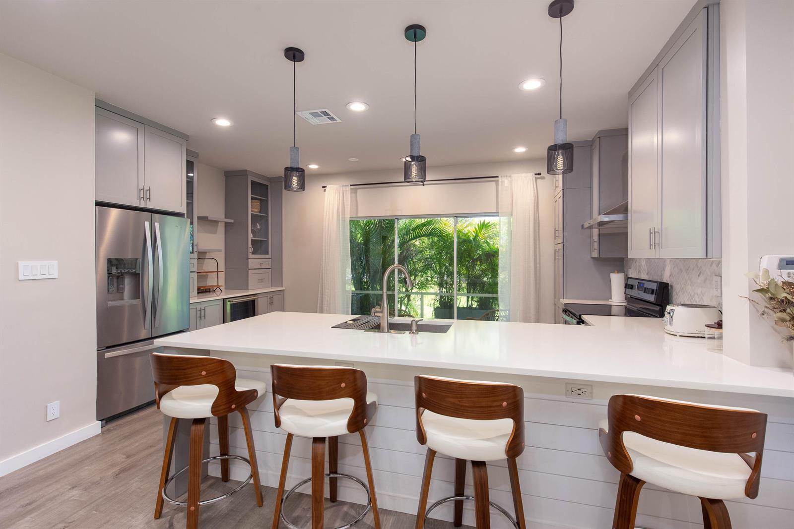 A modern kitchen features gray cabinetry, a white island with four barstools, and pendant lighting — 13792 Creston Place, Wellington FL 33414, WELLINGTON, FL