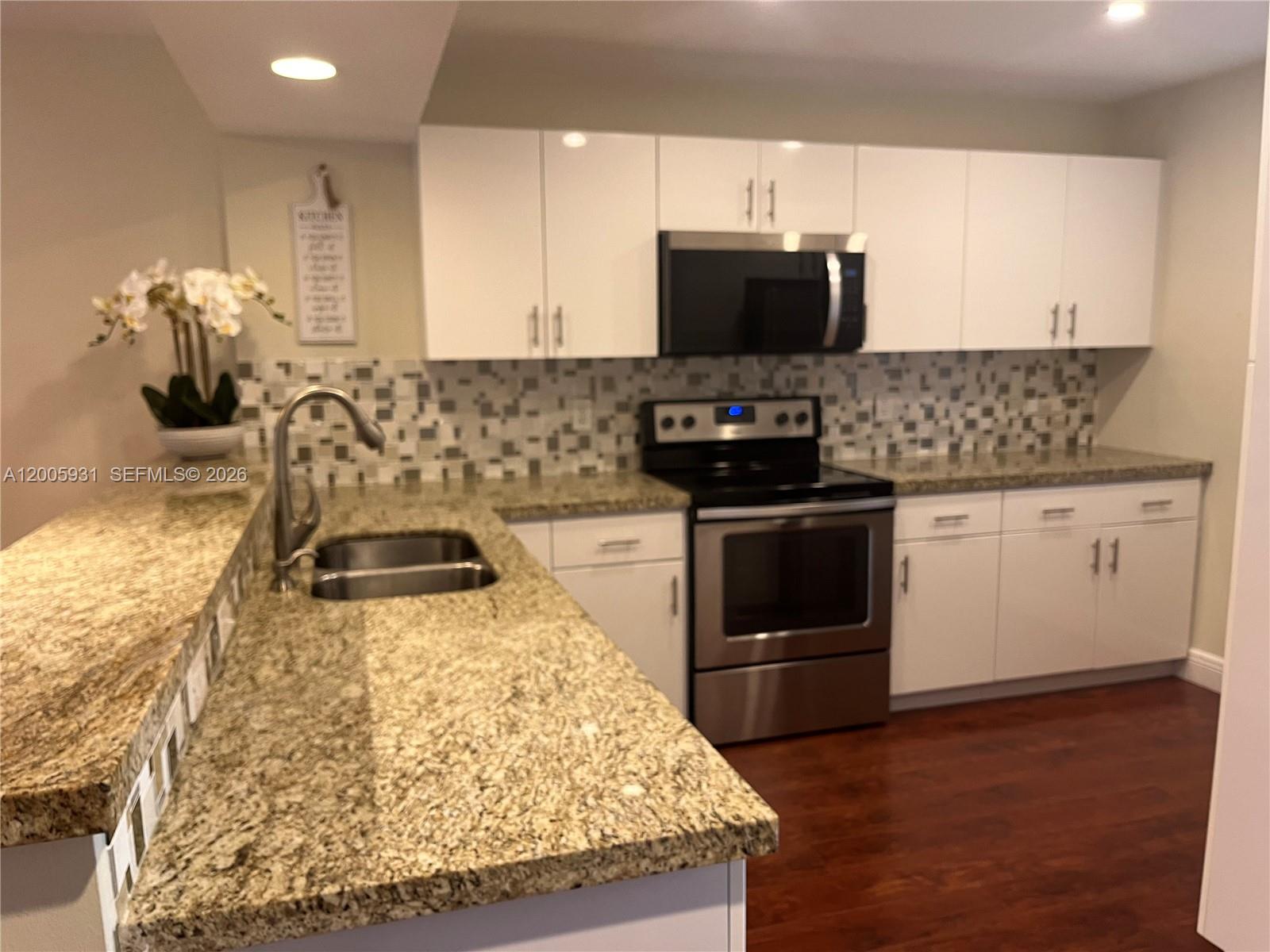 A kitchen features white cabinets, granite countertops, a stainless steel stove, and a mosaic backsplash — 201 Lakeview Drive # 204, Weston FL 33326, WESTON, FL