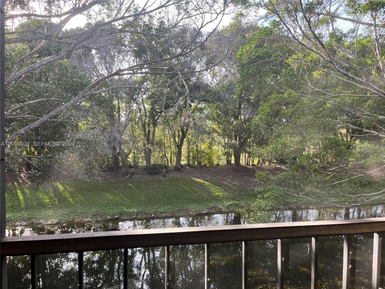 A view of a canal and wooded area from a screened-in balcony — 201 Lakeview Drive # 204, Weston FL 33326, WESTON, FL