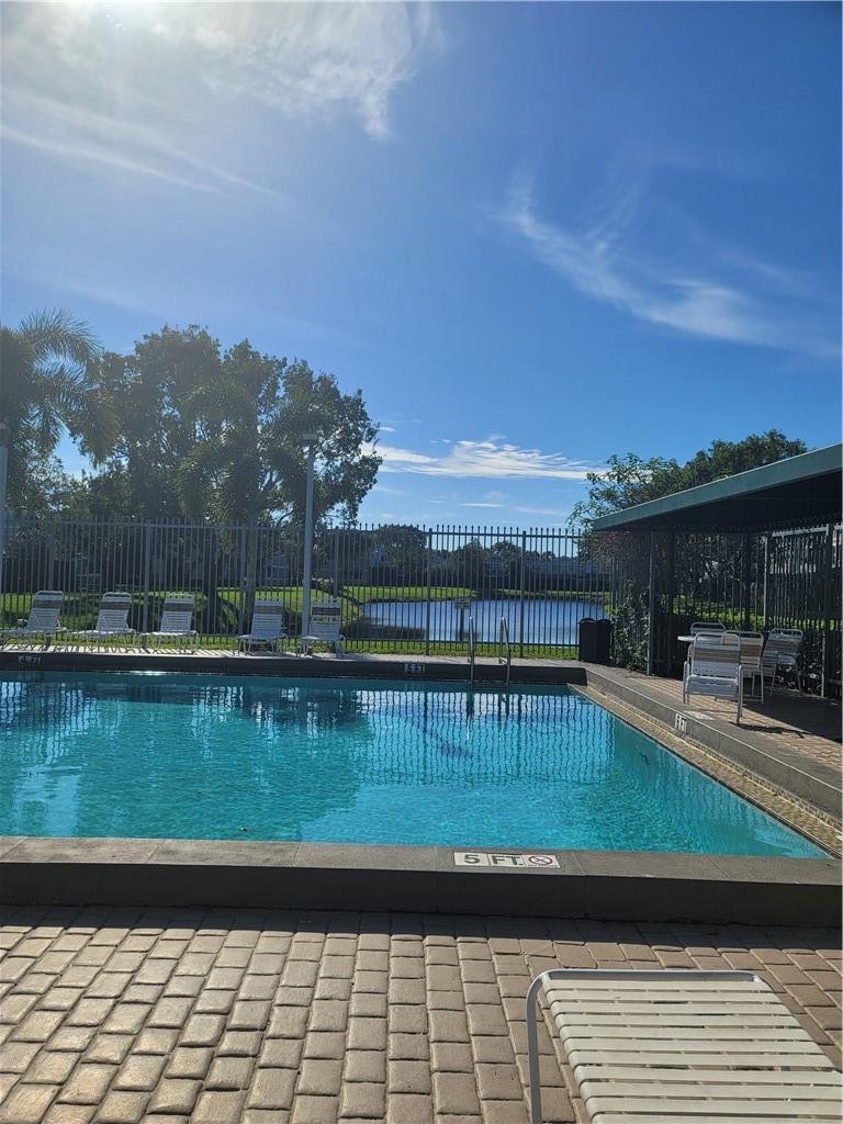 A swimming pool with a paved deck, lounge chairs, and a lake view in the background — 5200 Lake Loop Road, Cooper City FL 33330, COOPER CITY, FL