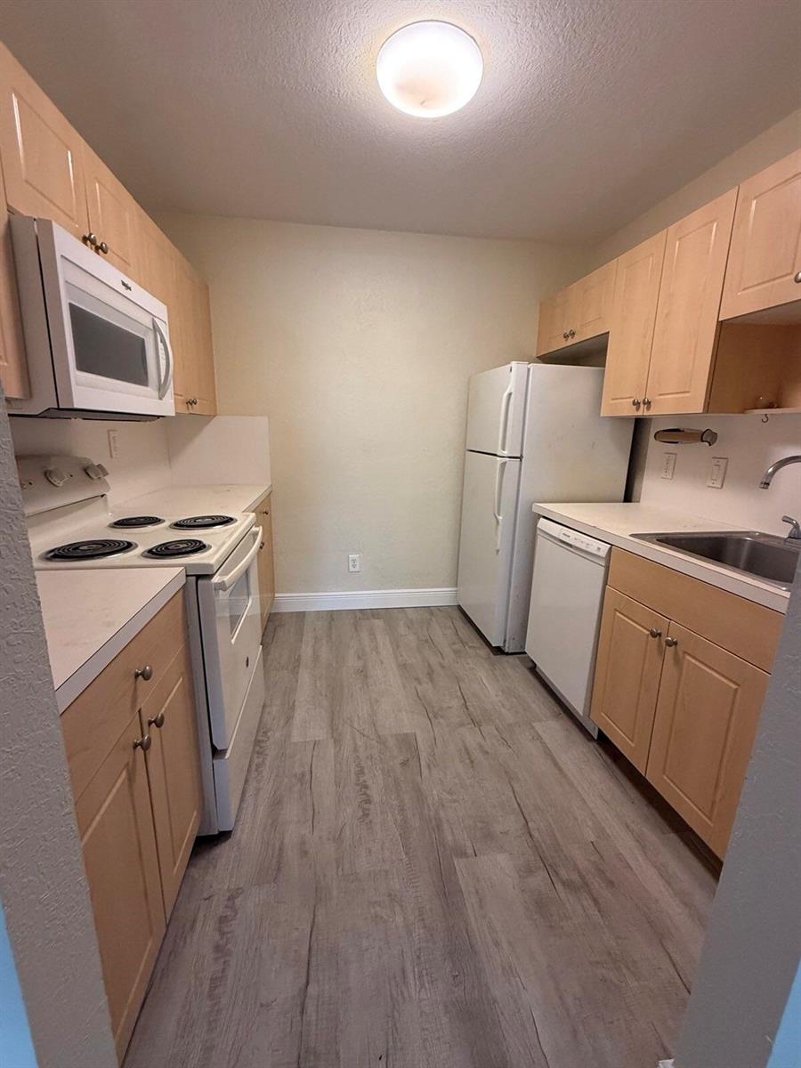 A galley kitchen features light wood cabinets, white appliances, and wood-look flooring — 760 SE 2nd Avenue # D112, Deerfield Beach FL 33441, DEERFIELD BEACH, FL