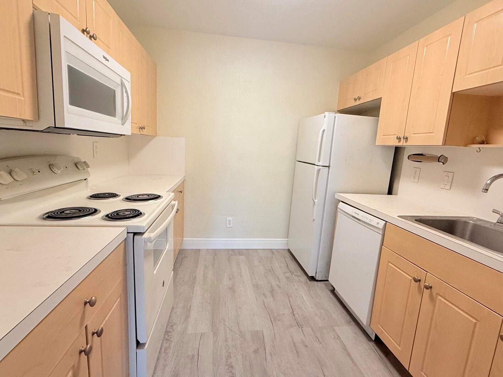 A galley kitchen features light wood cabinets, white appliances, and light-colored laminate flooring — 760 SE 2nd Avenue # D112, Deerfield Beach FL 33441, DEERFIELD BEACH, FL