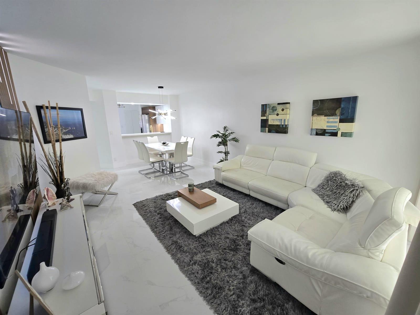 A living room with a white sectional sofa, gray rug, and an adjacent dining area — 5577 Courtyard Drive, Margate FL 33063, MARGATE, FL