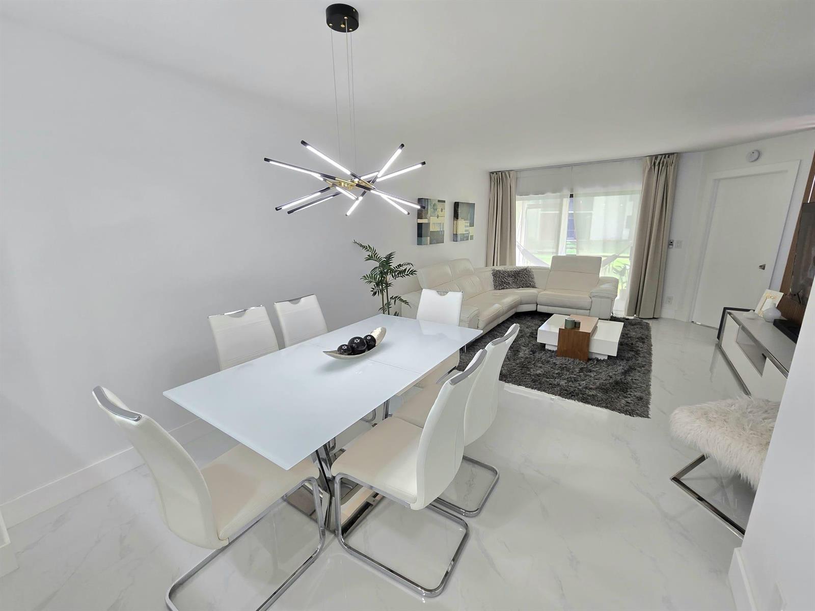 A modern open-concept dining and living area features white furniture, marble floors, and a chandelier — 5577 Courtyard Drive, Margate FL 33063, MARGATE, FL
