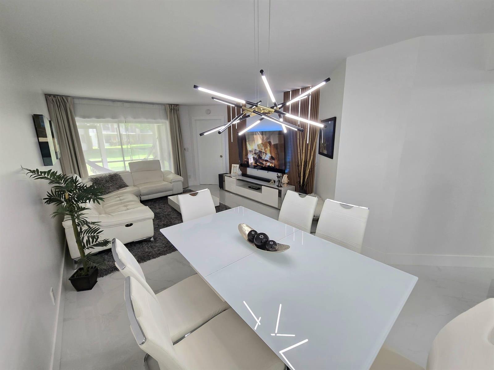 A modern dining area with a white table and chairs sits before a living room — 5577 Courtyard Drive, Margate FL 33063, MARGATE, FL