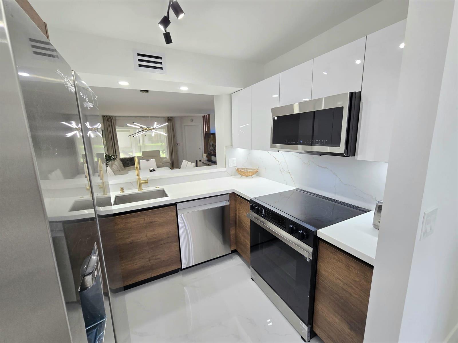 A modern kitchen features white glossy cabinets, wood-tone lower cabinets, stainless steel appliances, and countertops — 5577 Courtyard Drive, Margate FL 33063, MARGATE, FL