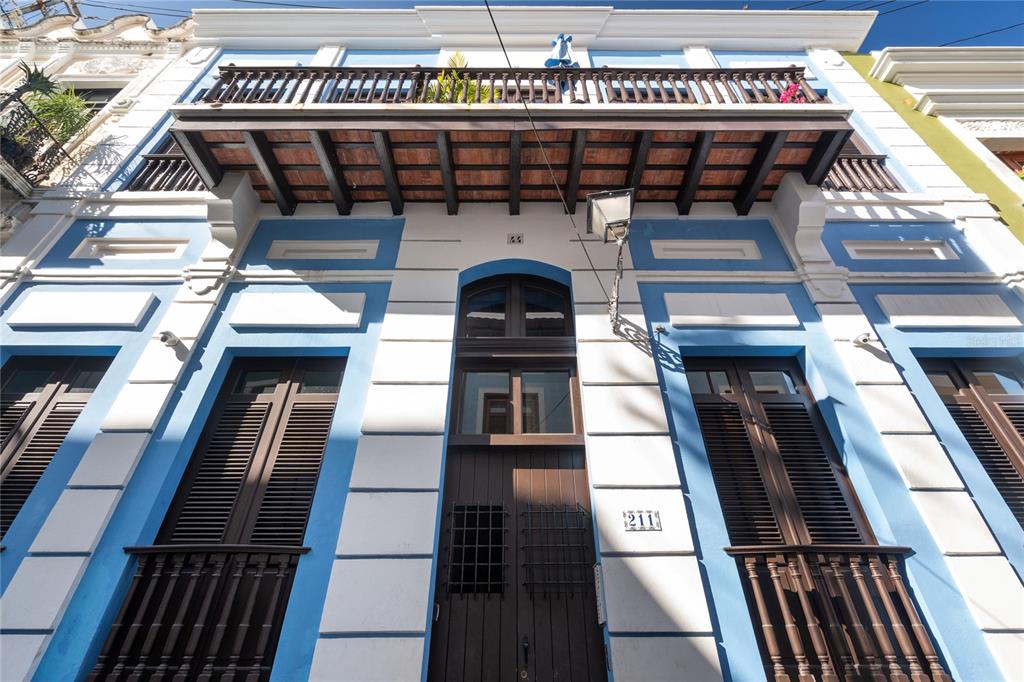 A low-angle view of a blue and white building facade featuring a wooden balcony — 211 Calle SOL PH UNIT 301, SAN JUAN, PR
