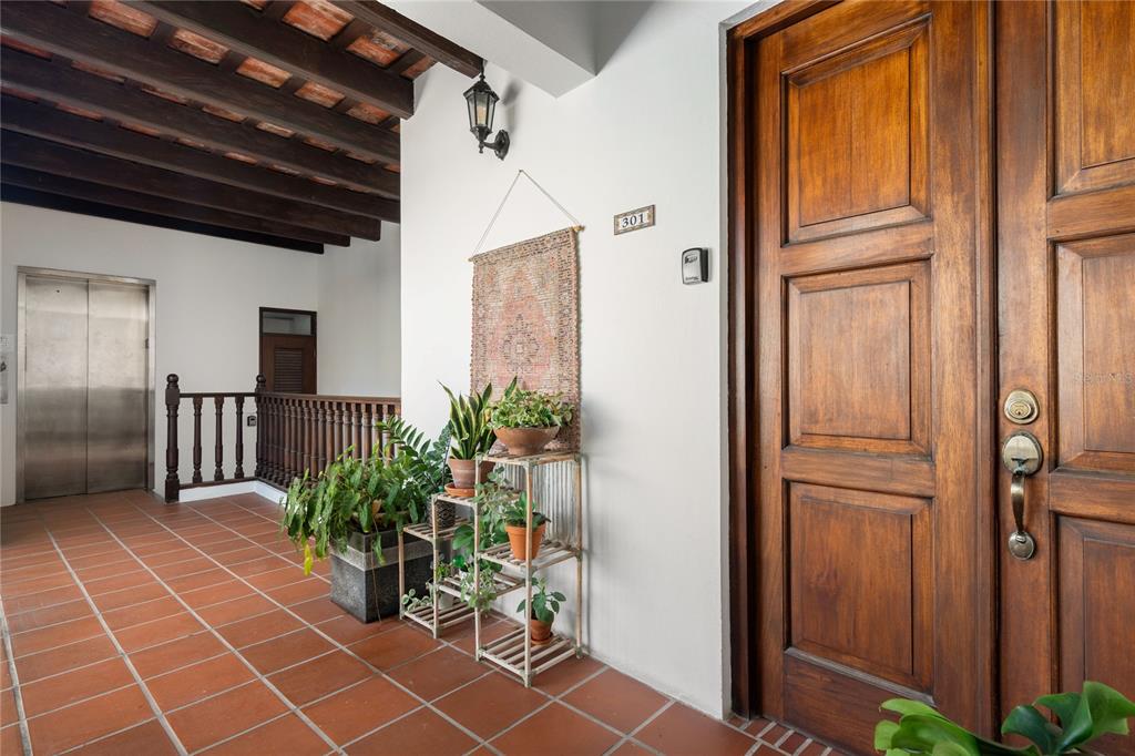 A hallway with terracotta tile flooring, exposed wooden ceiling beams, and a wooden entrance door — 211 Calle SOL PH UNIT 301, SAN JUAN, PR