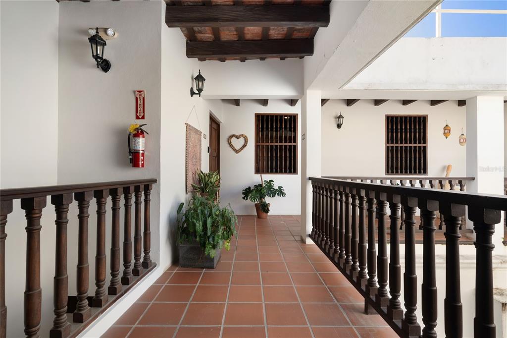 An outdoor hallway features terracotta tile flooring, dark wooden railings, and a wooden beamed ceiling — 211 Calle SOL PH UNIT 301, SAN JUAN, PR