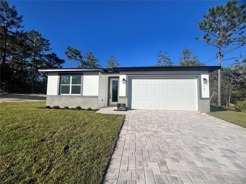 A single-story house with a white stucco exterior, a gray garage door, and a paver driveway — 3467 W SEAHORSE LANE, CITRUS SPRINGS, FL