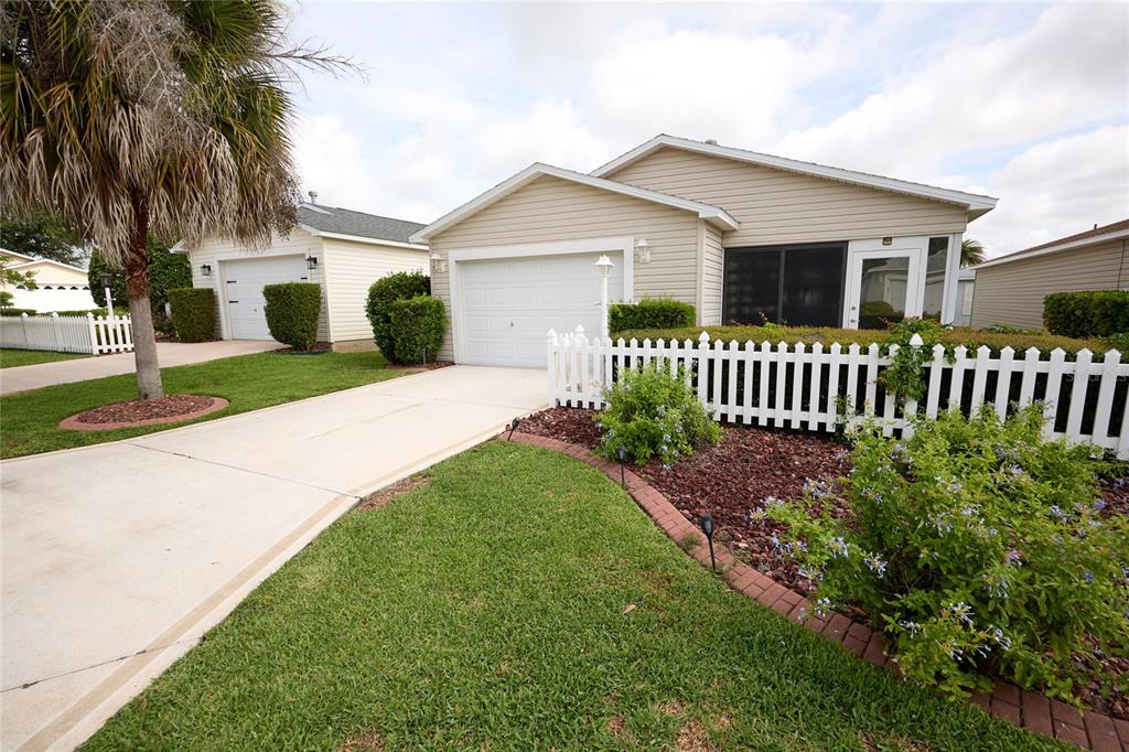 A beige single-story house with a white garage door, picket fence, and landscaped front yard — 2331 RILEY ROAD, THE VILLAGES, FL