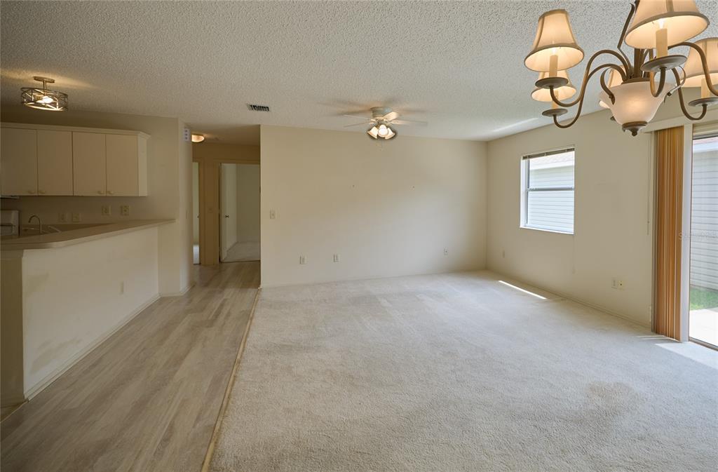An open-concept living room features beige carpet, a ceiling fan, and a dining area chandelier — 2331 RILEY ROAD, THE VILLAGES, FL