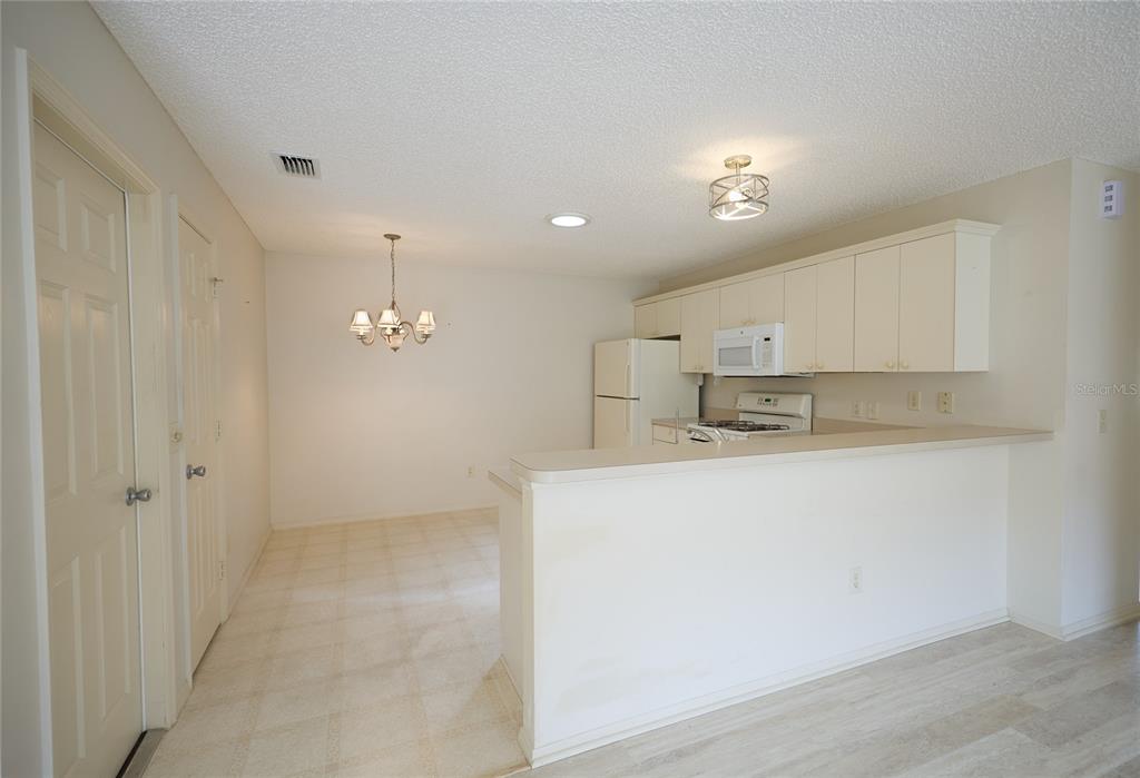 A kitchen with white cabinets and appliances overlooks a dining area with a chandelier — 2331 RILEY ROAD, THE VILLAGES, FL