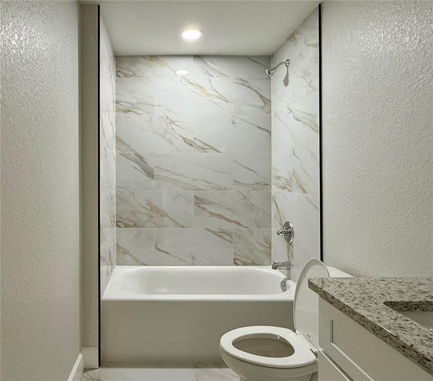 A bathroom features a white bathtub with marble-look tile walls and a nearby toilet — 1531 NE 153RD AVENUE, WILLISTON, FL