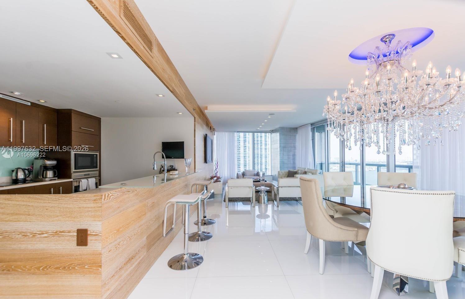 A modern open-concept dining and kitchen area features a large crystal chandelier and bar seating — 465 Brickell Ave # 2301, Miami FL 33131, MIAMI, FL