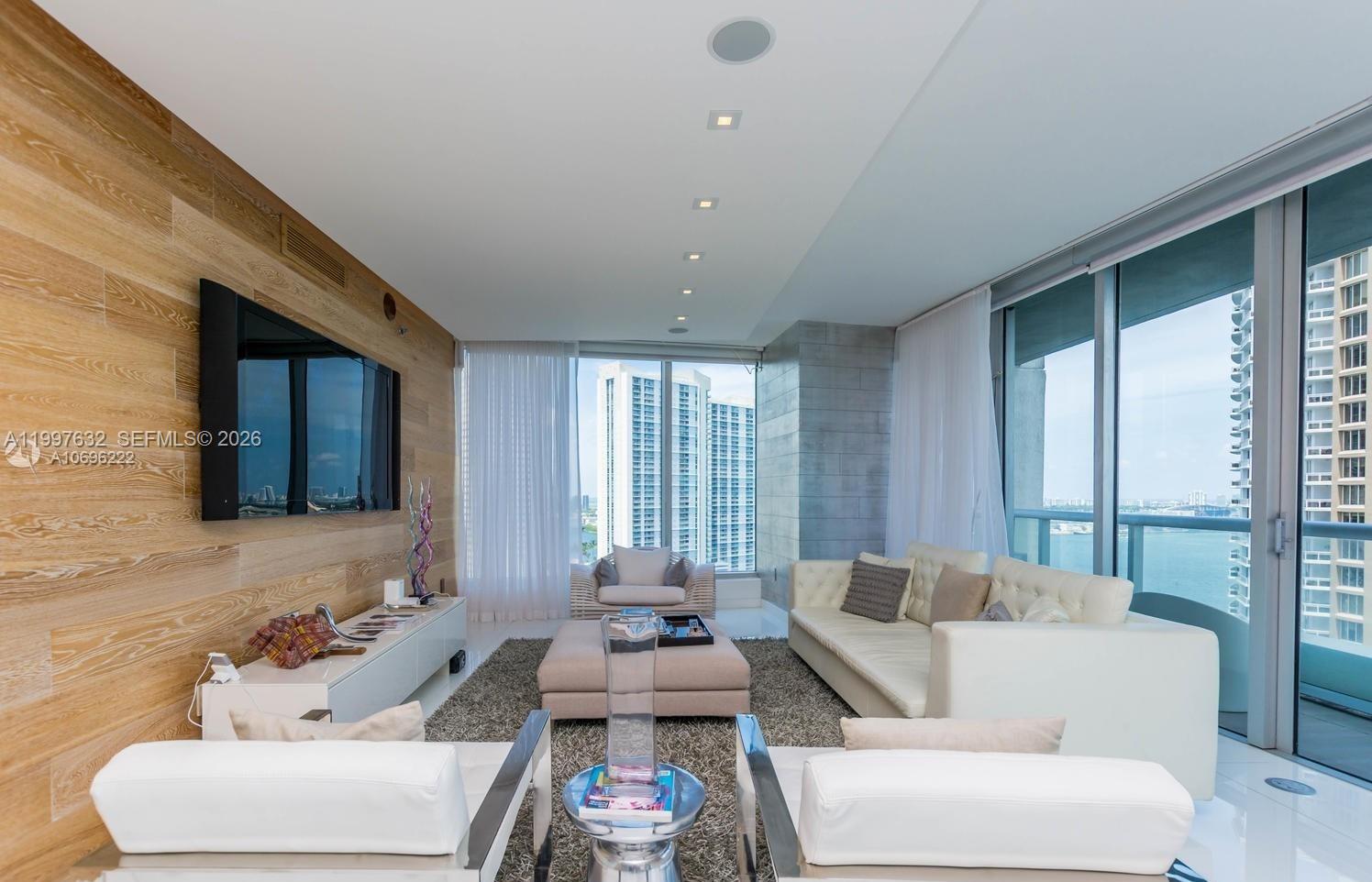 A modern living room features a wood-paneled wall, white furniture, and floor-to-ceiling windows with views — 465 Brickell Ave # 2301, Miami FL 33131, MIAMI, FL