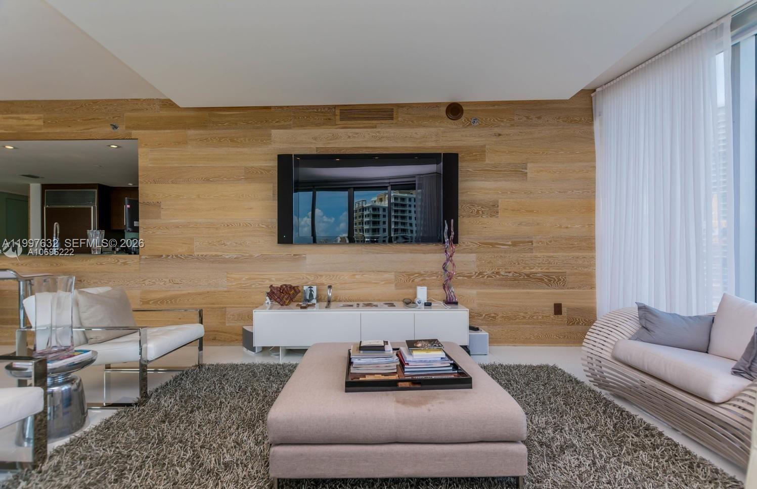 A living room features a wood-paneled accent wall, a wall-mounted television, and a central ottoman — 465 Brickell Ave # 2301, Miami FL 33131, MIAMI, FL