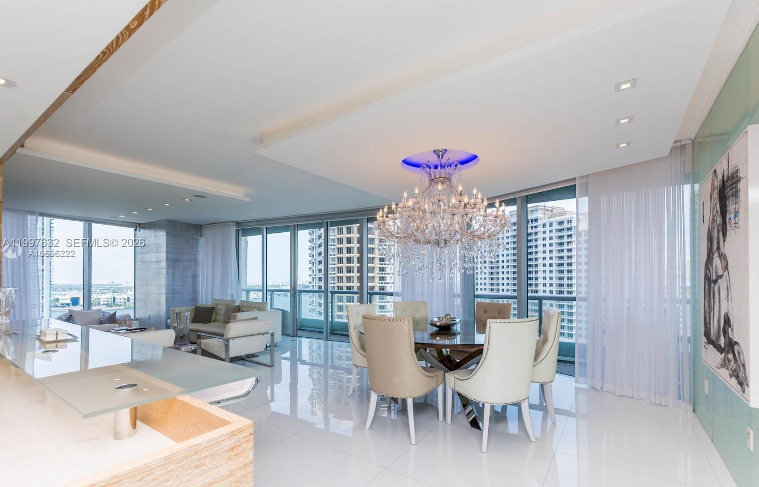 A dining area with a crystal chandelier, glass table, and floor-to-ceiling windows overlooking city buildings — 465 Brickell Ave # 2301, Miami FL 33131, MIAMI, FL