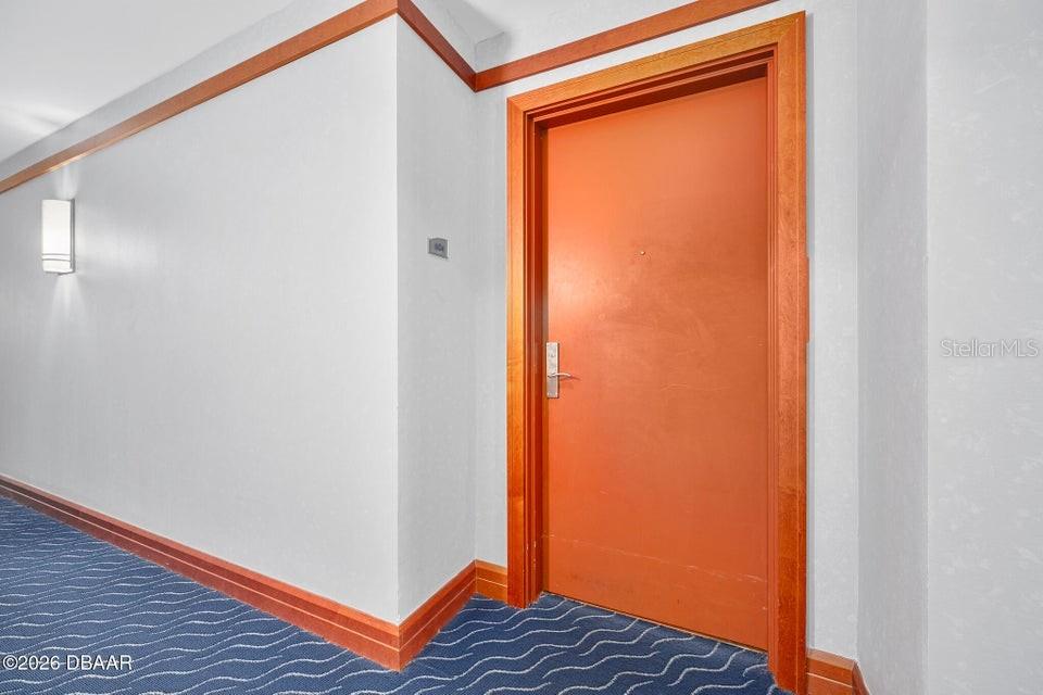 A hallway features a solid orange door with wood trim, a wall sconce, and blue carpet — 231 RIVERSIDE DRIVE UNIT 604-1, HOLLY HILL, FL