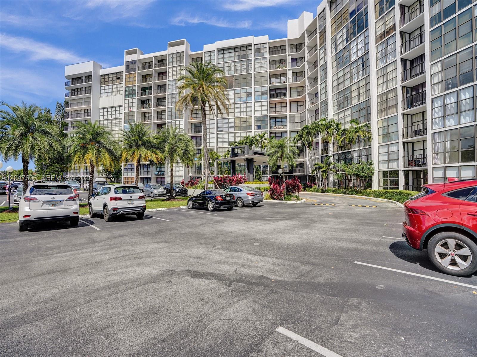 A multi-story apartment building features a parking lot with several cars in the foreground — 800 Parkview Dr # 131, Hallandale Beach FL 33009, HALLANDALE BEACH, FL