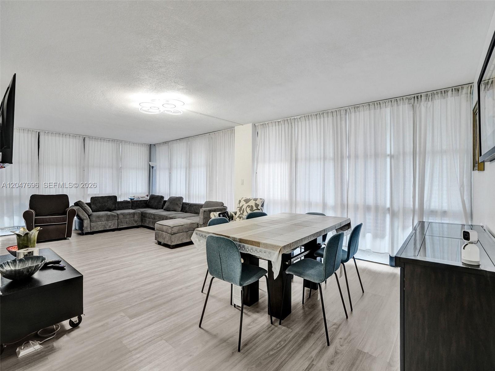 A living and dining area features light wood flooring, floor-to-ceiling curtains, and modern furniture — 800 Parkview Dr # 131, Hallandale Beach FL 33009, HALLANDALE BEACH, FL