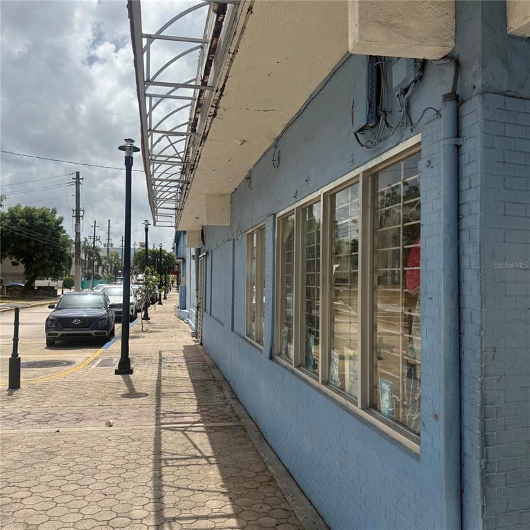 A blue brick building exterior features large display windows along a paved sidewalk — AVE. COMERIO ESQ. BETANCES, BAYAMON, PR