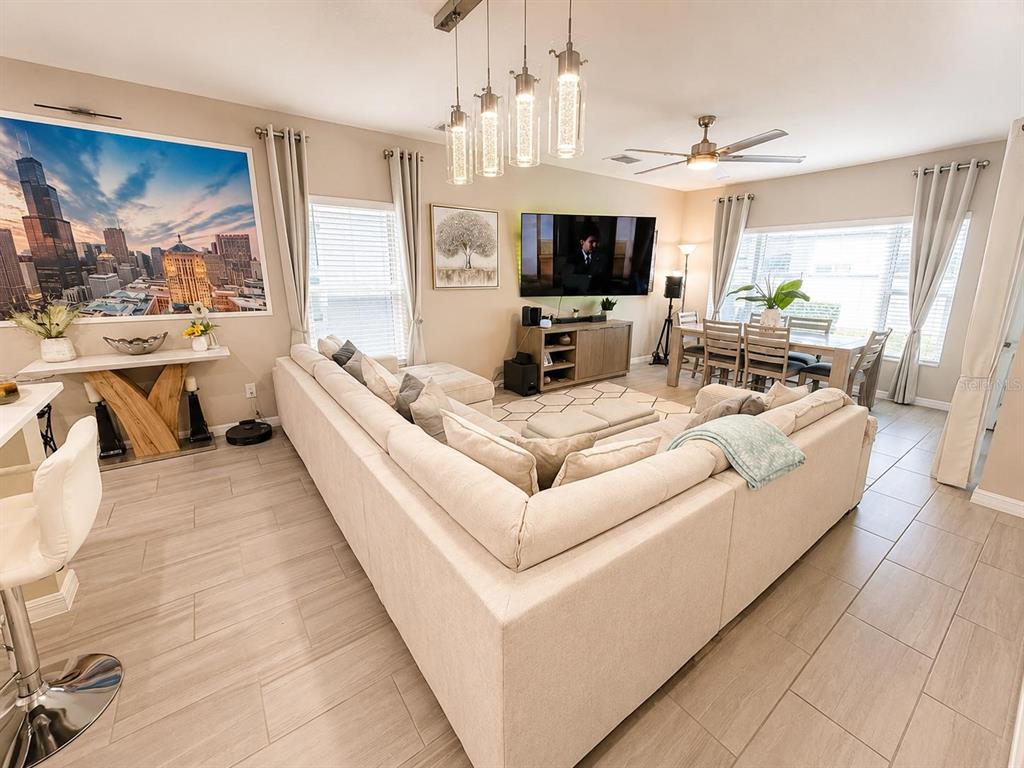 An open-concept living and dining area features a large sectional sofa, tile flooring, and pendant lighting — 1254 WISPY CYPRESS DRIVE, KISSIMMEE, FL