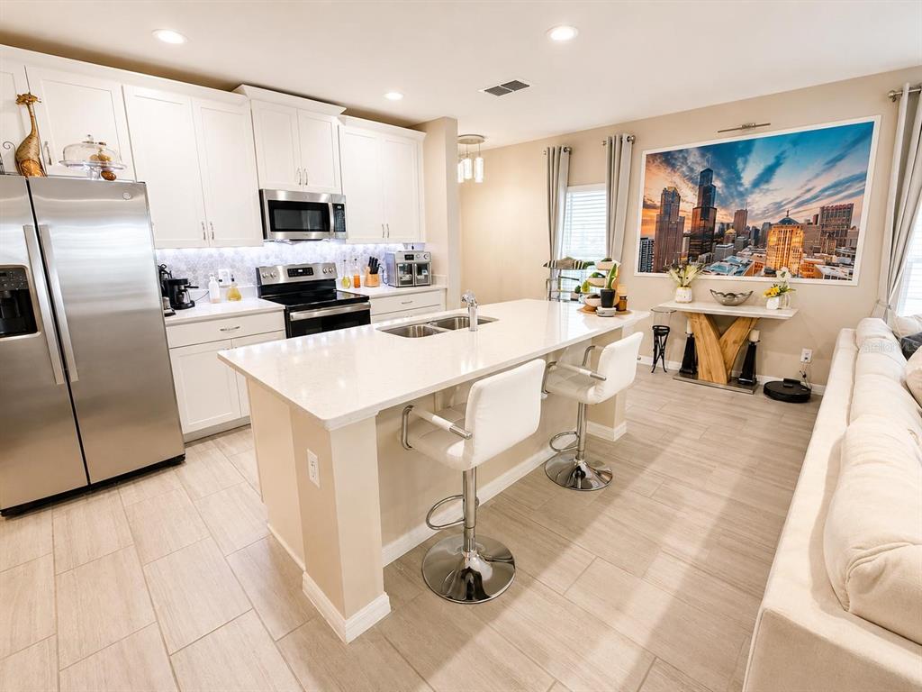 A modern kitchen features white cabinetry, stainless steel appliances, a quartz island, and tile flooring — 1254 WISPY CYPRESS DRIVE, KISSIMMEE, FL