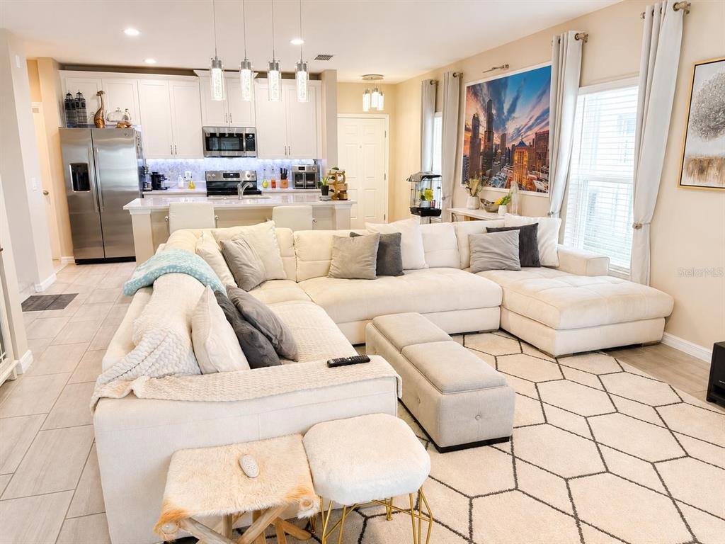 A living room with a large white sectional sofa opens to a modern kitchen — 1254 WISPY CYPRESS DRIVE, KISSIMMEE, FL